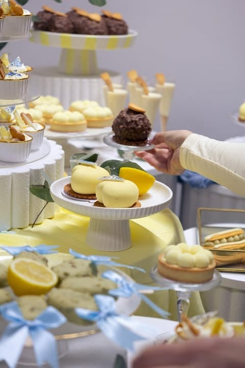 Hand picking up a chocolate truffle from a dessert display with yellow and white themed pastries and treats