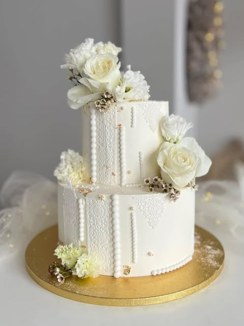 Three-tiered white wedding cake with cream roses and gold accents on a gold base plate